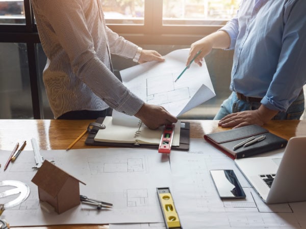 Two architects collaborating on blueprints at a desk.