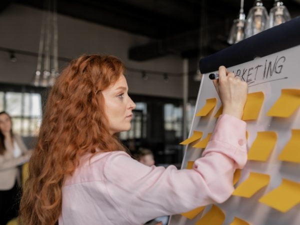 A woman using sticky notes on a whiteboard to plan architectural designs.