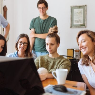 A group of students gathered around a table engaged in educational activities on a laptop.