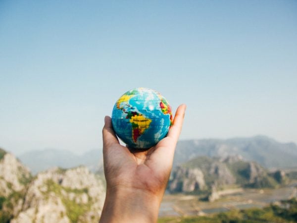 A traveler's hand holding a globe with mountains in the background.