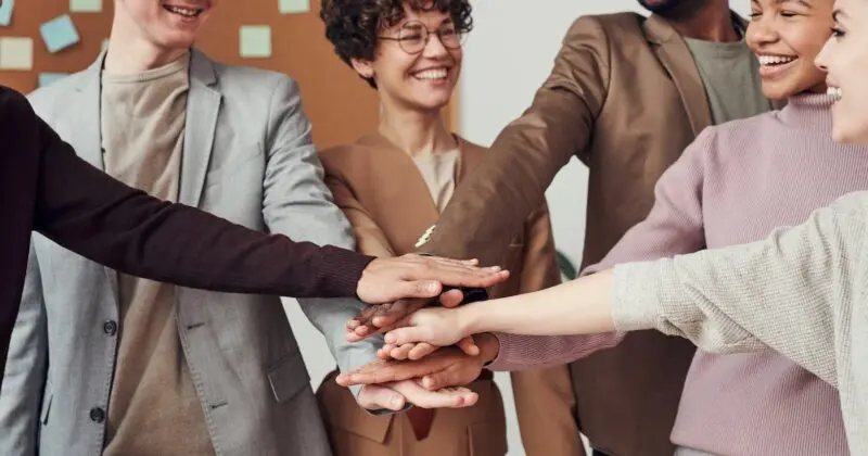 A circle of individuals charting direction in a unified mission, with their hands put together.