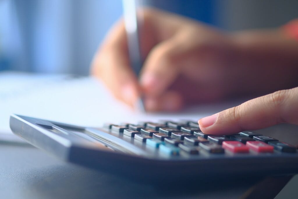 A person is using a calculator to solve the Magic Marketing Equation on a desk.